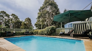Una piscina con sillones de descanso y una zona cubierta.