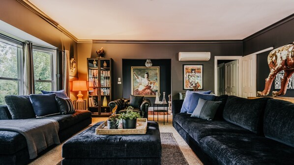 Una sala de estar con un sofá oscuro, una estantería, un cuadro y una estatua decorativa de un caballo.