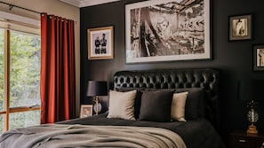 A bedroom with a large bed, a window with red curtains, and framed pictures on the wall. - Istana Lodge - 5 Bed house on acreage with pool (Musk Vale)