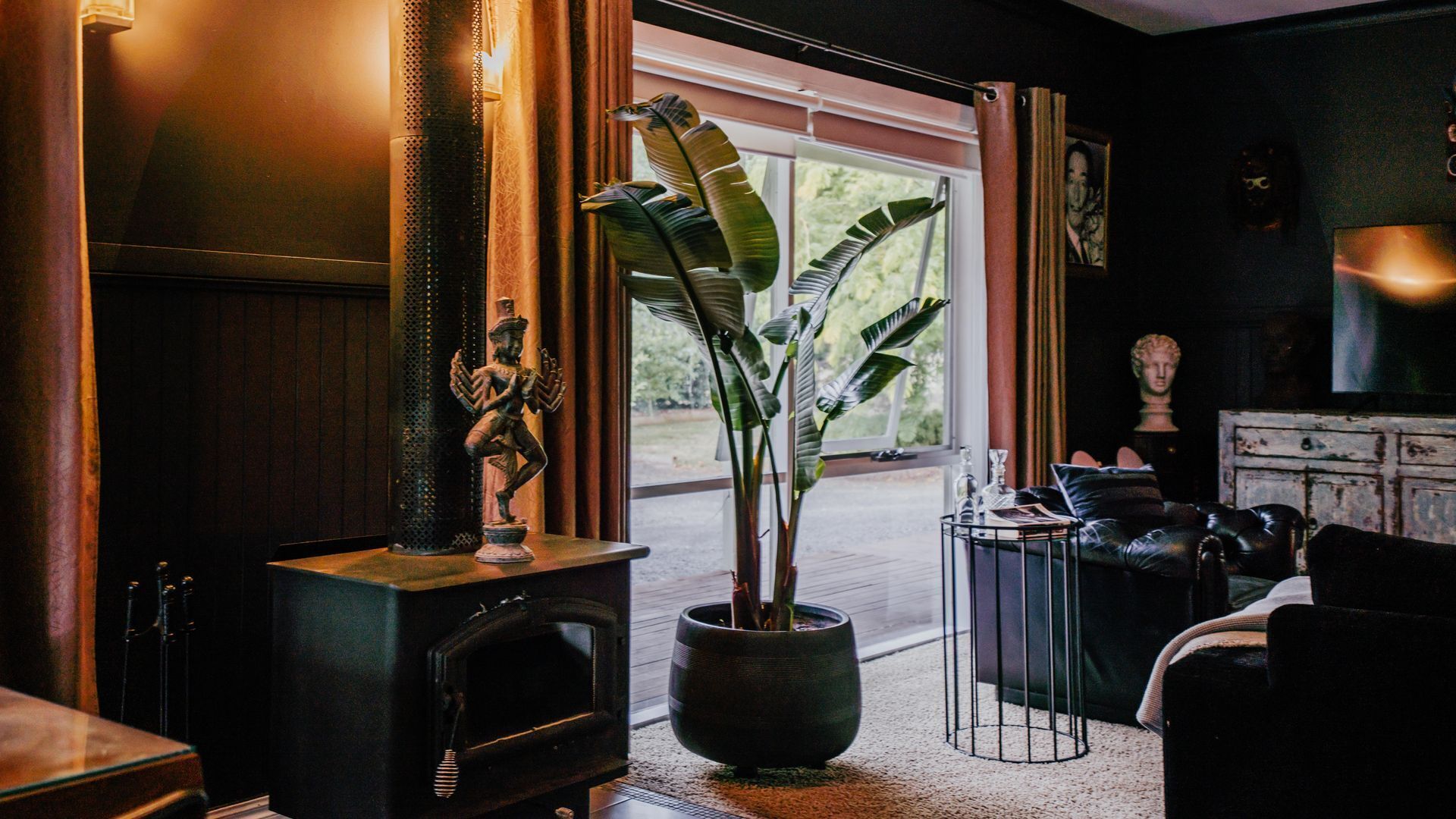 A room with a fireplace, a potted plant, a statue, and a view of the outdoors.