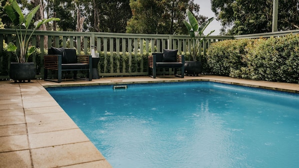 A rectangular swimming pool with a tiled deck, surrounded by a green fence and lush greenery. - Istana Lodge - 5 Bed house on acreage with pool (Musk Vale)
