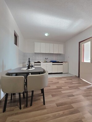 Uma cozinha compacta com armários brancos, uma mesa de jantar com cadeiras e piso de madeira.