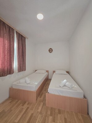 Quarto com duas camas de solteiro, piso de madeira, janela com cortinas e luminária no teto.