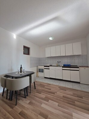 A compact kitchen with white cabinets, a dining table with chairs, and a small window. - Apartment & Rooms Tempera / Apartment 1 (Neum)