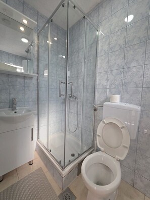 Uma casa de banho moderna com chuveiro em cabine de vidro, lavatório branco e sanita.