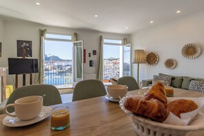 A dining area with a table set for breakfast, a TV, and a view of the city. - The "Classé VIP", a balcony perched on the Old Port (La Ciotat)