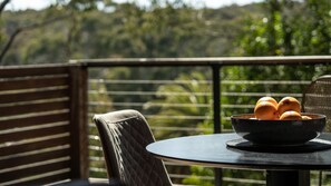 Una mesa redonda con un cuenco de naranjas en un balcón con vistas a árboles.