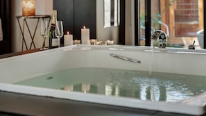 Un baño moderno con una bañera grande, una copa de vino, una botella de champán y velas.