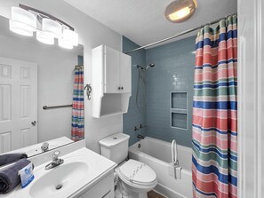 Ein Badezimmer mit einem weißen Waschbecken, einer Toilette und einer Badewanne, einem gestreiften Duschvorhang und einem Spiegel über dem Waschbecken.