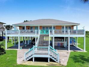 A two-story building with a covered front porch, a staircase, and a mural. - Pelican and Palms 3 bed 2.5 baths Sleeps 14 Ocean View 3 minute walk to beach (Crystal Beach)