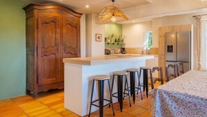 A kitchen with a wooden cabinet, a bar stool area, a refrigerator, and a dining table.