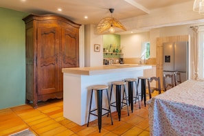 Une cuisine équipée d’un meuble en bois, d’un coin bar avec des tabourets, d’un réfrigérateur et d’une table à manger.