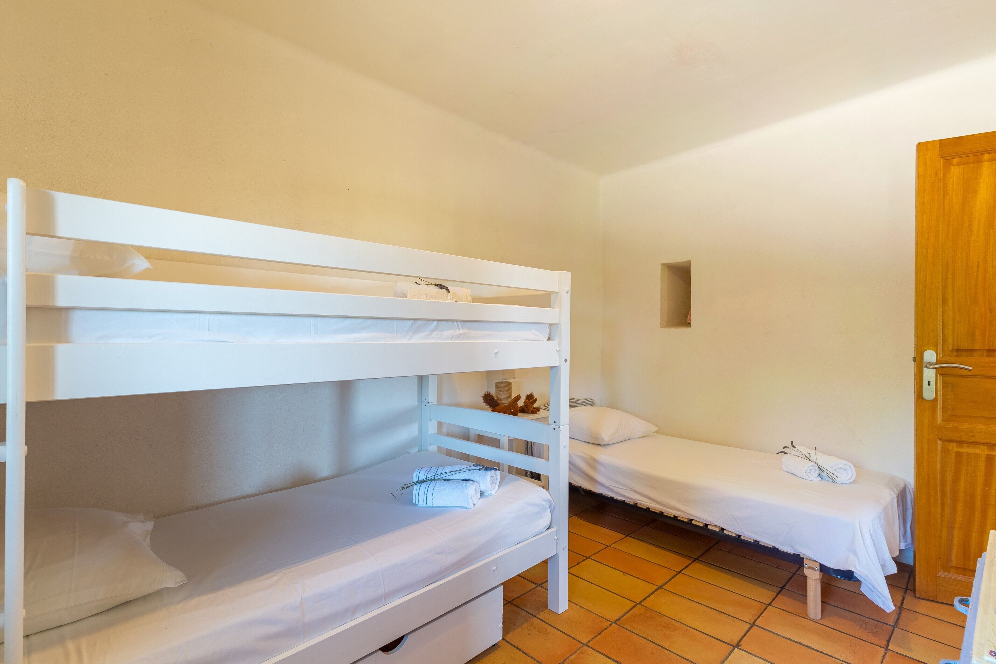 Ein Zimmer mit Etagenbetten, einem Einzelbett, einer Holztür und einem Fliesenboden.