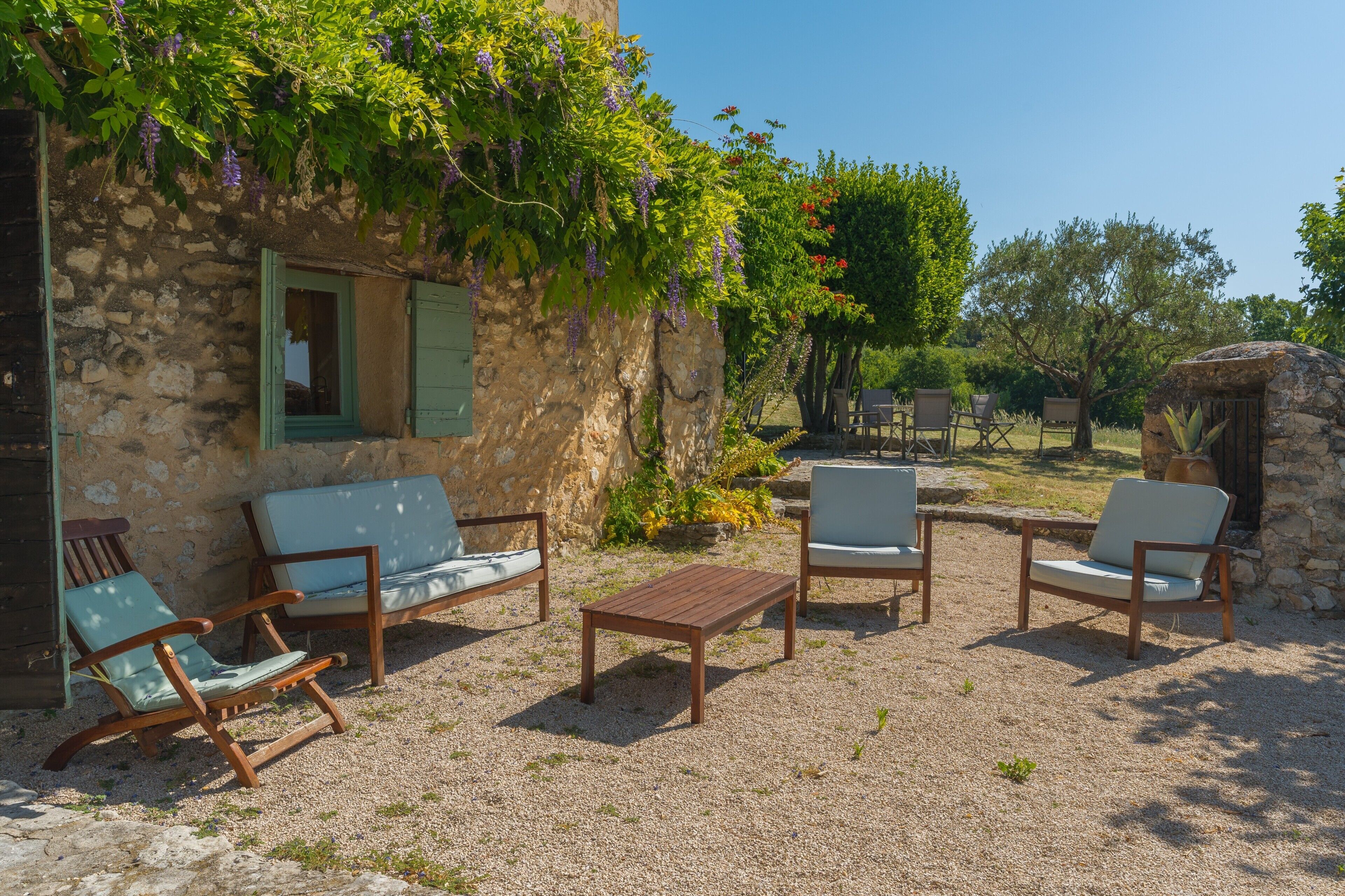Un edificio de piedra con un área de estar rústica al aire libre que incluye una mesa y sillas de madera, todo rodeado de grava.