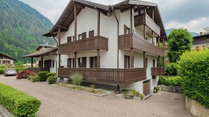 Un edificio a più piani con balconi, un vialetto lastricato e vegetazione circostante.
