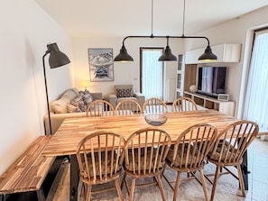 Ein Essbereich mit Holztisch und -stühlen, einem Sofa, einer Lampe und einem Bild an der Wand.