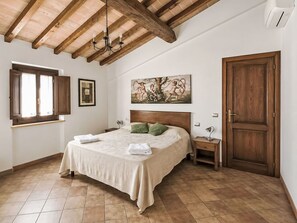 Ein Schlafzimmer mit Holzbalkendecke, einem Bett mit grünem Kopfkissen, einem Nachttisch, einem Gemälde und einer Tür.