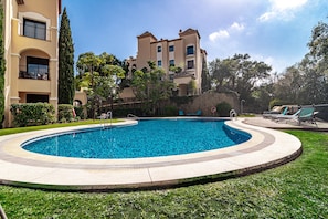 A swimming pool with a curved design, surrounded by a well-maintained lawn and a multi-story building with balconies. - BVQ - Stunning Sea & Golf View Terrace (Benahavis)