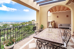 A balcony with a tiled table and chairs, a sofa, and a view of the city. - BVQ - Stunning Sea & Golf View Terrace (Benahavis)