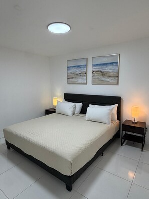 A bedroom with a bed, two bedside lamps, a ceiling light, and two framed pictures on the wall. - BEACHFRONT 2 bedroom CONDO-HOTEL with parking and direct beach access (Miami Beach)