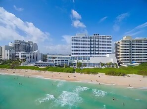 A beachfront hotel with multiple high-rise buildings, a sandy beach, and clear turquoise waters. - BEACHFRONT 2 bedroom CONDO-HOTEL with parking and direct beach access (Miami Beach)