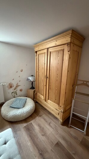 Ein Zimmer mit Holzschrank, rundem Hocker, Lampe und Heizkörper.