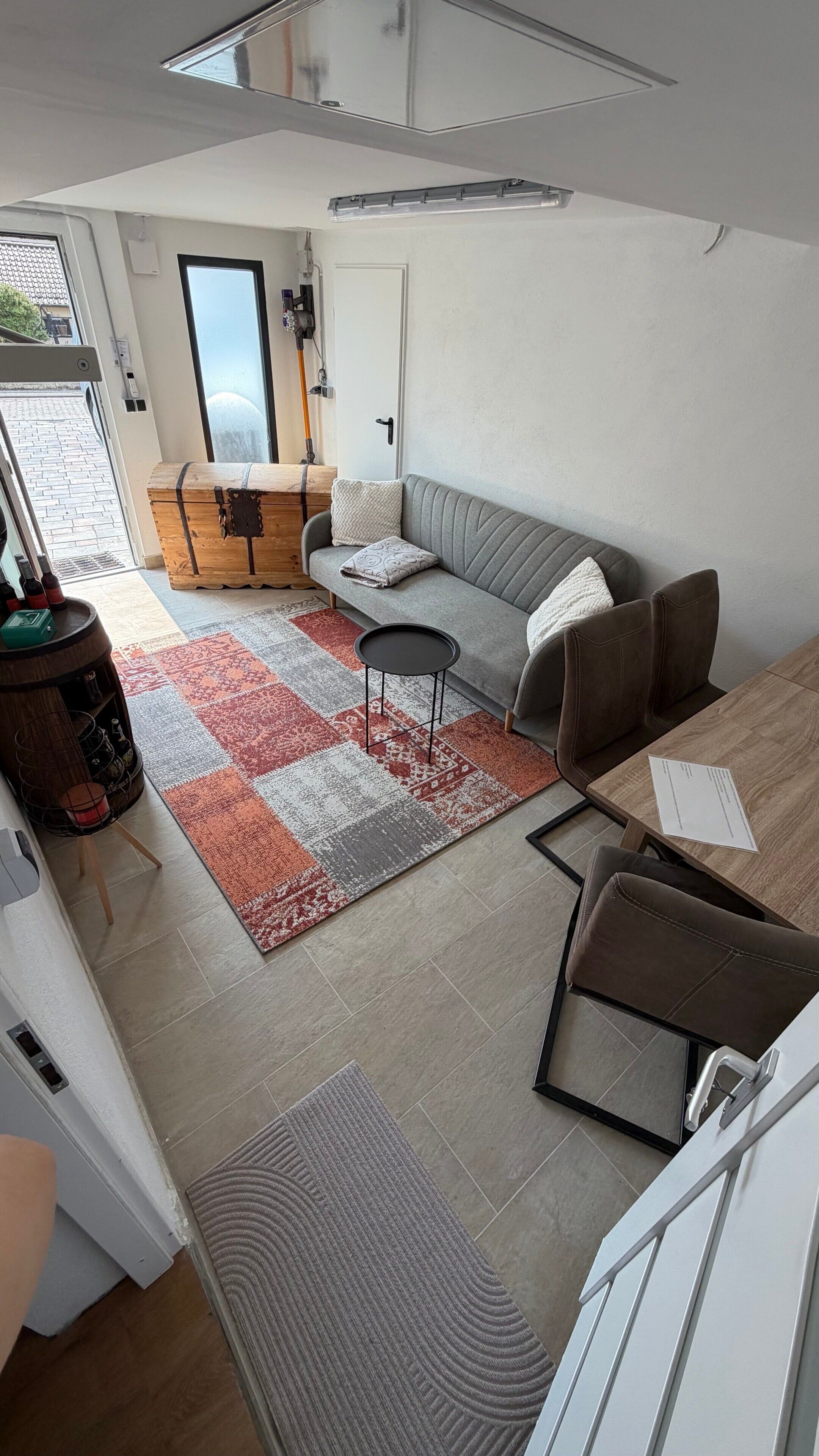 Ein modernes Wohnzimmer mit einem grauen Sofa, einem kleinen runden Tisch und einem gemusterten Teppich.