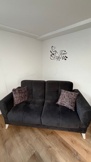 Um sofá preto com duas almofadas xadrez em frente a uma parede branca, com um adesivo decorativo acima.