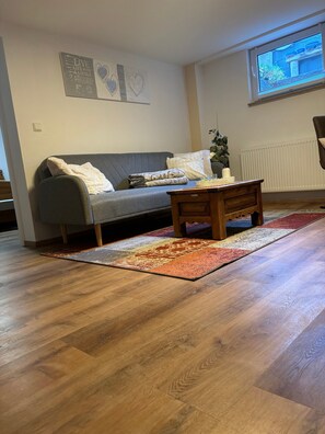 Ein Wohnzimmer mit grauem Sofa, einem Holztisch und einem gemusterten Teppich.