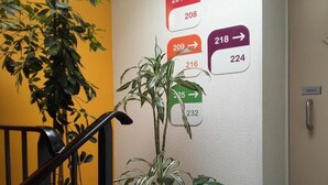 A staircase with a potted plant, a wall with numbered room signs, and a door labeled 'TIREEZ'.