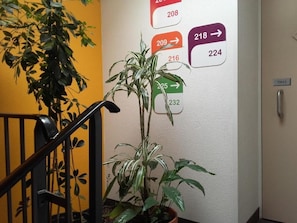 A staircase with a potted plant, a wall with numbered room signs, and a door labeled 'TIREEZ'. - UNISOTEL-MONTAUBAN (Montauban)