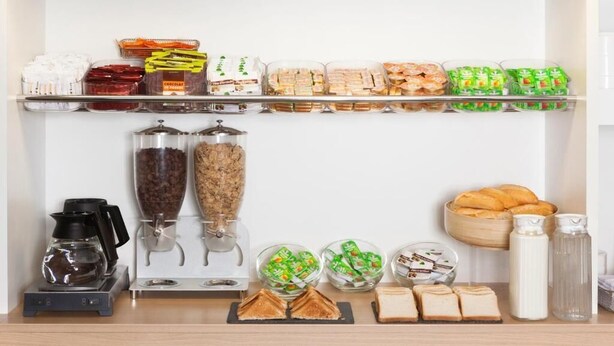 A breakfast bar with various food items, a coffee machine, and condiments.