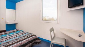 A bedroom with a bed, a desk, a chair, a TV, and a window.