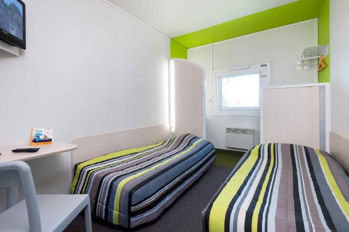 Una habitación pequeña y luminosa con dos camas, un escritorio y una ventana.