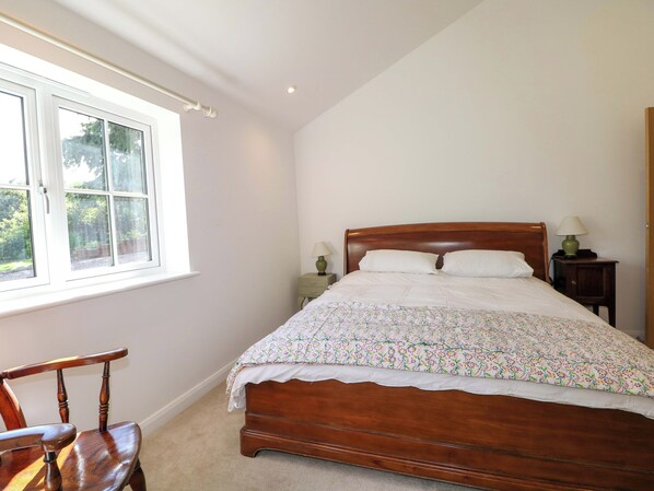 A bedroom with a wooden bed, a window, a chair, and a nightstand with a lamp.