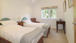 Un dormitorio con dos camas, una ventana con vista a árboles, una mesita de noche con lámpara y una pequeña mesa con una caja.