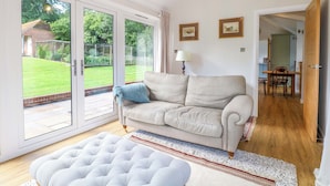 A living room with a sofa, a lamp, a rug, and a view through a glass door to a garden. - Keepers Cottage (Haslemere)