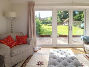 A living room with a sofa, ottoman, and a view through a sliding glass door to a garden.