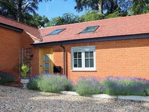A brick house with a red tiled roof, a wooden door, and a window with white frames. - Keepers Cottage (Haslemere)