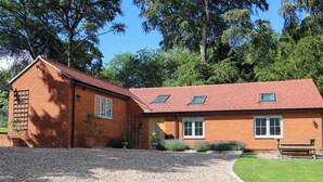 A brick house with a gravel driveway, a wooden bench, and a garden. - Keepers Cottage (Haslemere)