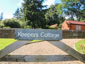A wooden gate with a sign that reads 'Keepers Cottage.'