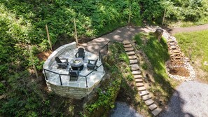 A stone-built outdoor seating area with a fire pit and chairs, surrounded by a stone wall and lush greenery. - The Acosta (Maggie Valley)