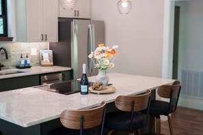 A modern kitchen with a marble countertop, wooden chairs, a wine bottle, and a vase with flowers. - The Acosta (Maggie Valley)