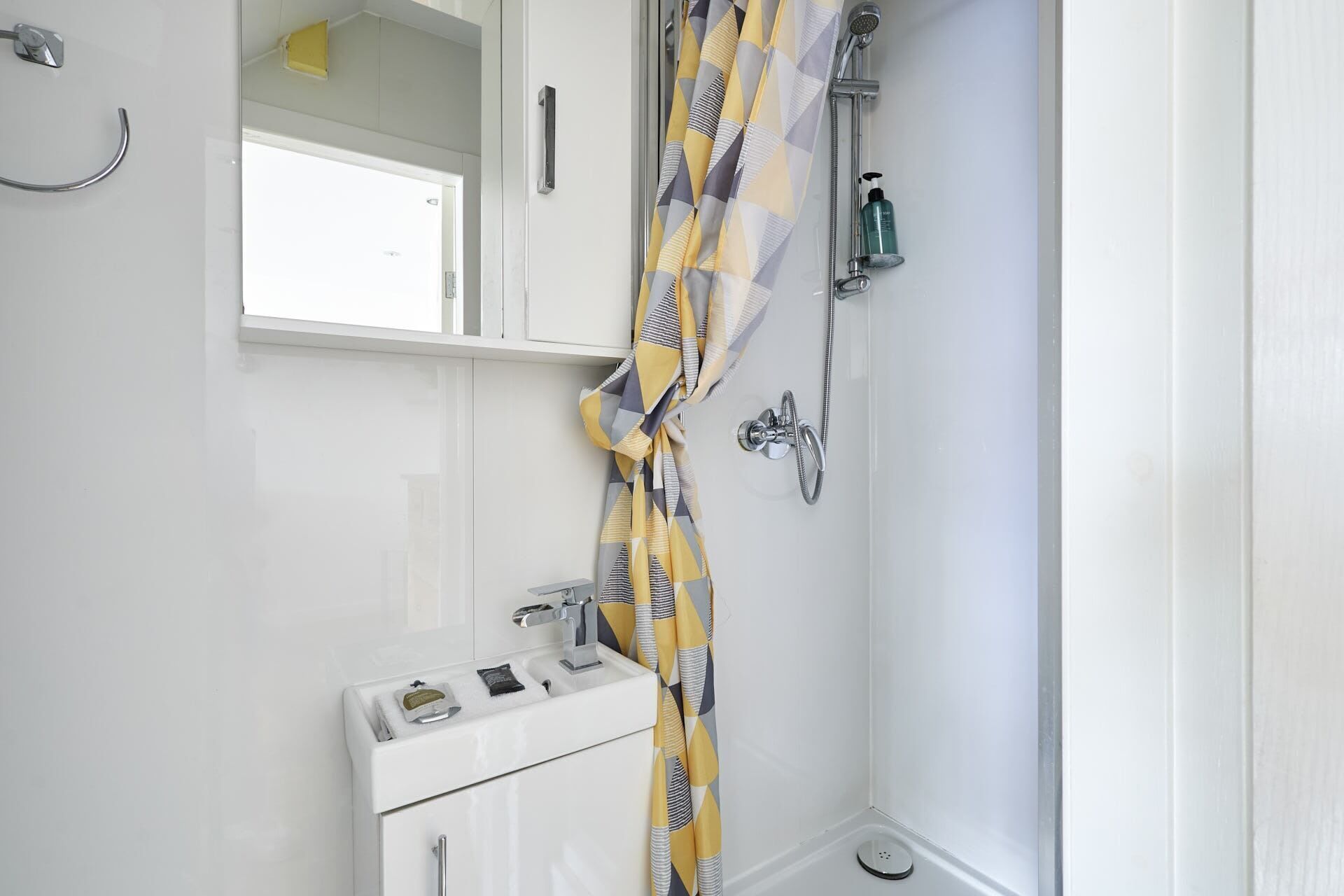 Een badkamer met een witte wastafel, een spiegel, een douche met een decoratieve gordijn en een toilet.