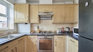 A kitchen with wooden cabinets, a gas stove, an oven, a microwave, and a refrigerator. - Host & Stay | Urban Nest LIV (Liverpool)