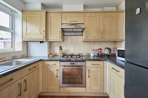 Eine Küche mit Holzschränken, einem Gasherd, einem Backofen, einer Mikrowelle und einem Kühlschrank.
