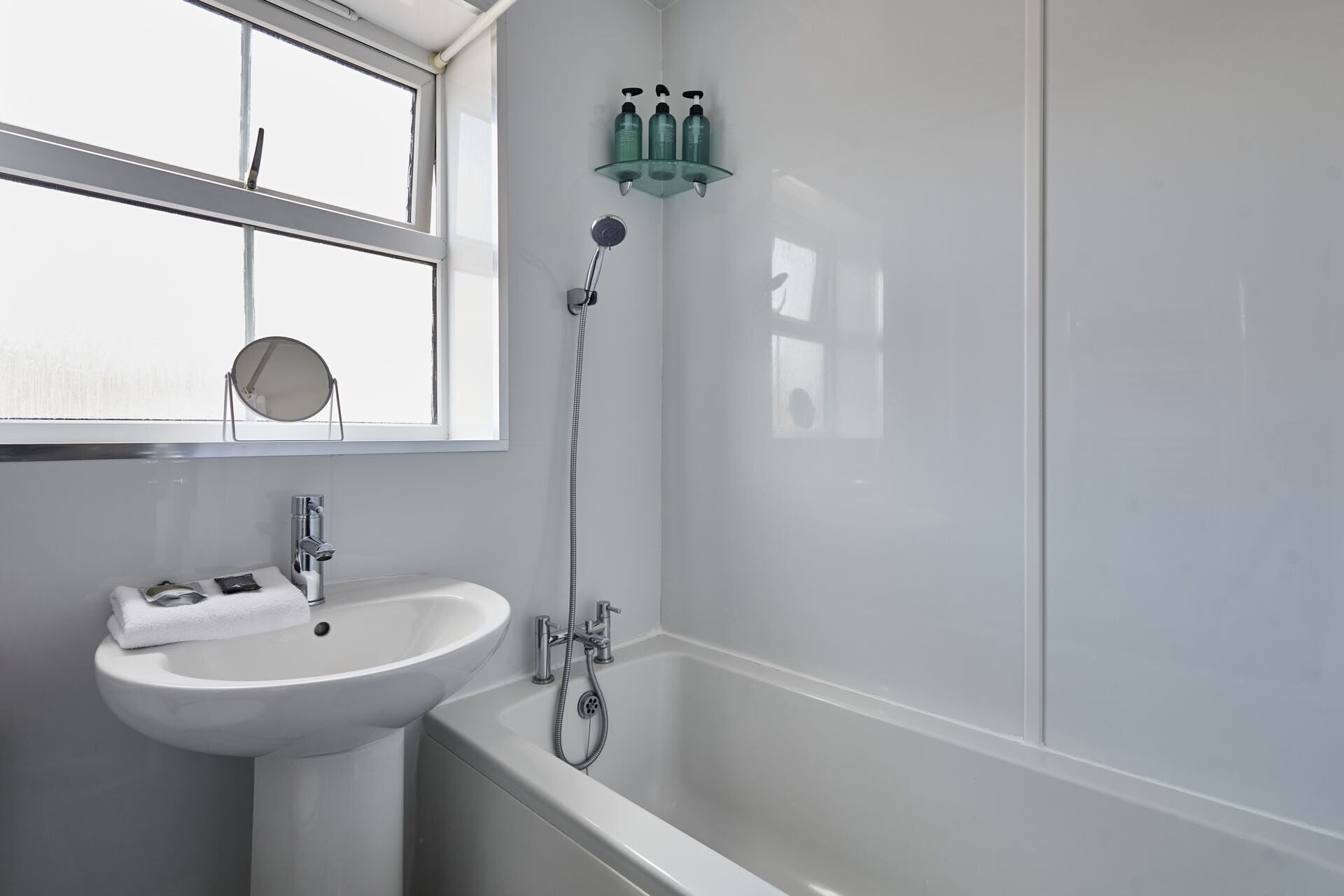 Un bagno con un lavandino bianco, uno specchio, una finestra e una doccia.