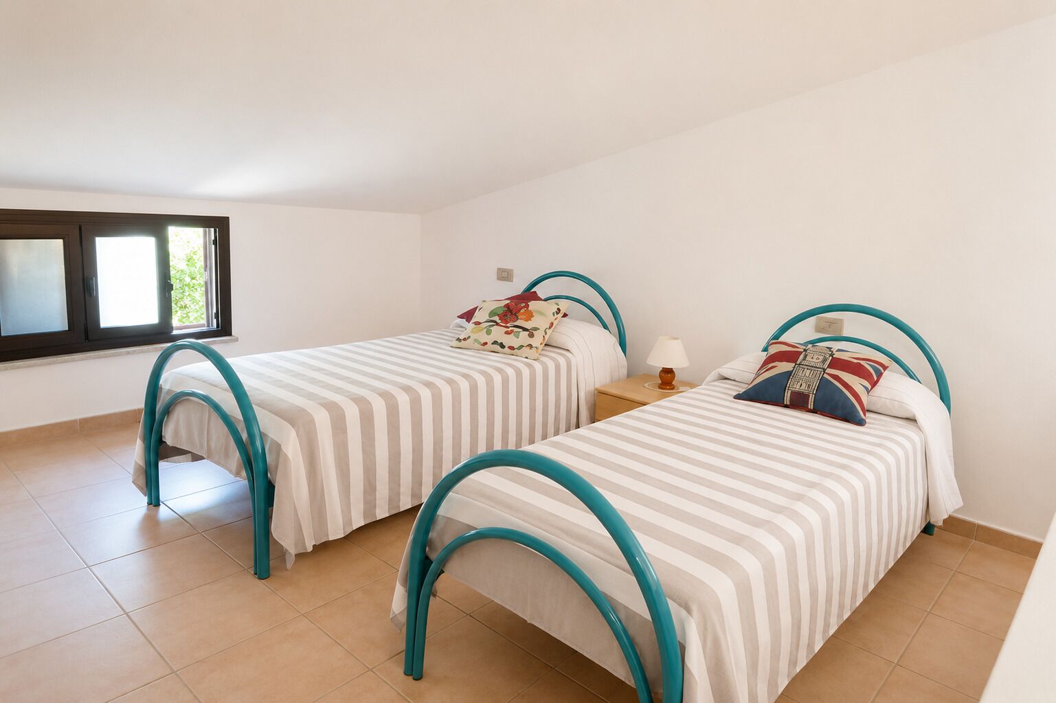 A room with two beds, each with a curved headboard, a window, and a tiled floor.
