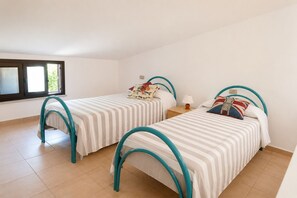 Quarto com duas camas, cada uma com cabeceira curvada, uma janela e chão em mosaico.