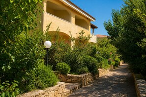 Un chemin menant à un bâtiment dont le mur est en pierre et qui est bordé de chaque côté par de la verdure.